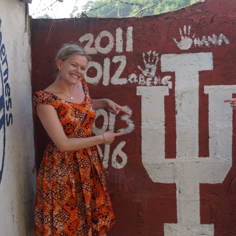Dana Vanderburgh poses in front an IU trident mural painted in Ghana and visited by each year's visitors from IU.